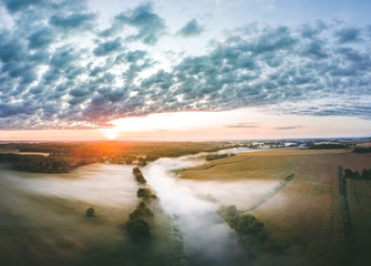  Aerial view over a misty morning over countryside. Fog covering the crop fields and river....
