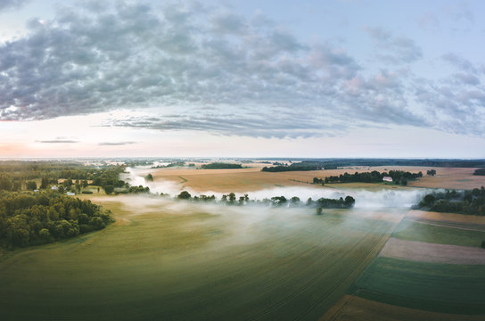  Aerial view over a misty morning over countryside. Fog covering the crop fields and river. Colorful sunrise over the fields and forest. 