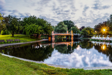 Boston Public Garden park bridge crossing reflective pond smooth with image of sky.