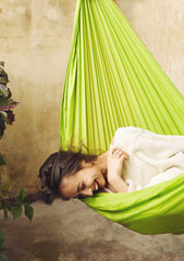 Happy young woman relaxing in a hammock on the terrace house. Woman lying and covered with plaid in a hammock. Concept of rest, enjoyment, carefree.