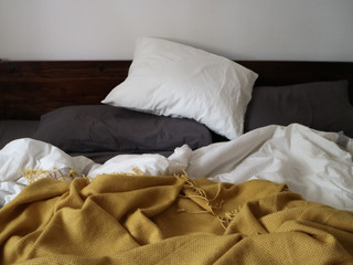 Messy bed in the morning with white an grey sheets and pillows