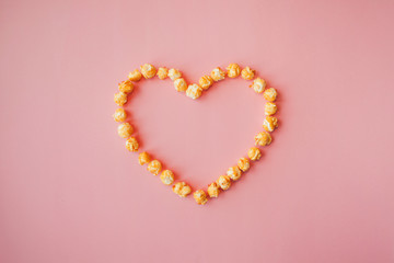 Love movies, concept on a pink background. Popcorn scattered on pink background heart shaped