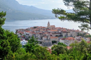 Obraz premium A view from afar looking down through the trees from a lookout of the beautiful ancient Croatian town of Korcula, on Korcula Island in the Adriatic sea off the coast of Croatia
