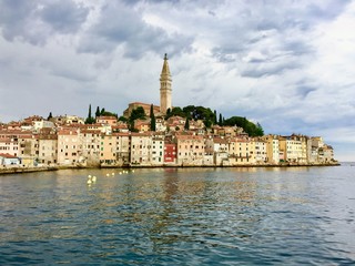 Fototapeta na wymiar A view from the ocean facing the old town of Rovinj, Croatia. Old colourful buildings and the clock tower dominate the skyline facing the beautiful adriatic sea.