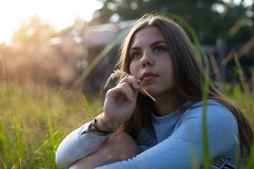 Teenage girl sitting in green grass in summer countryside.