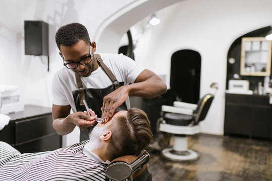 Man getting his beard shaved with razor in barber shop