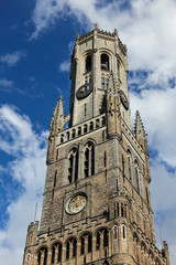 Fototapeta na wymiar Bruges, Flanders, Belgium - June 16, 2019: Brown-gray Brick stone Top of the tower of the Belfry against blue sky with white clouds.