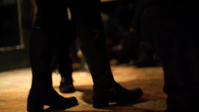 Guitarist plays to bar patrons by night. A ground level view on the feet of a group of people dancing and tapping feet on the wooden floor of a public house by night.