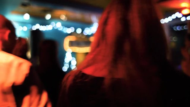 Guitarist plays to bar patrons by night. Low angle shots of happy people dancing along to live music inside a crowded bar by night. Celebratory people let their hair down.