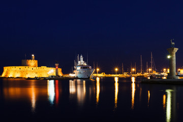 Night photo of ancient fortress and pier in Rhodes city on Rhodes island, Dodecanese, Greece. Stone walls and bright night lights. Famous tourist destination in South Europe