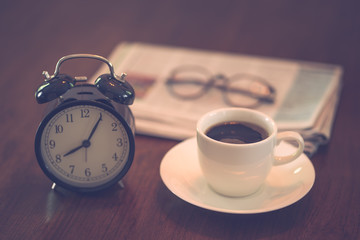 Fototapeta na wymiar Hot coffee cup and vintage clock newspaper reading glasses on brown wood table