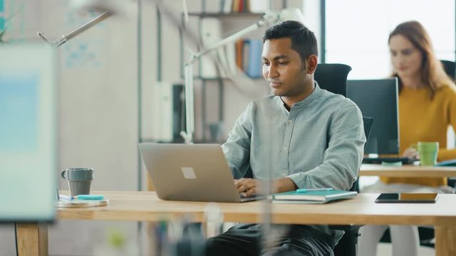 Handsome Indian Information Technology and Brilliant Female Data Specialist Sitting at Their Desks work on Desktop Computers. Modern Office with Diverse Team of Young Professionals Working
