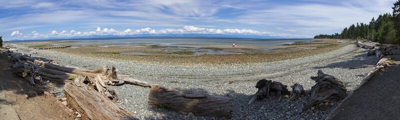 Wide Panoramic Scenic Landscape View of Miracle Beach BC Provincial Park during low tide on Vancouver Island looking across Strait of Georgia towards distant Cloud Covered Sunshine Coast Mountain Peak