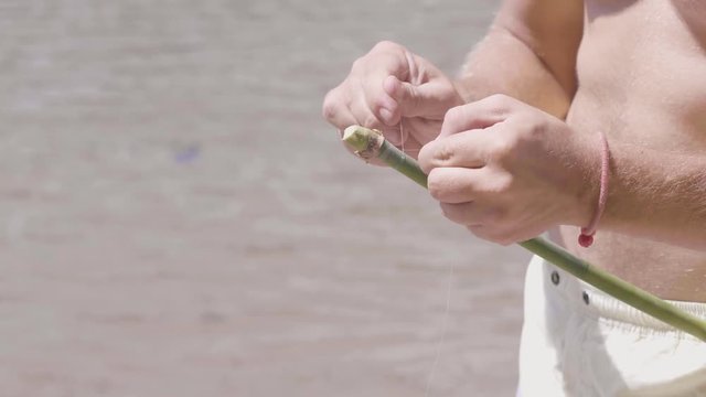 Man ties a fishing line to the edge of bamboo stick, handmade fising rod, hands closeup