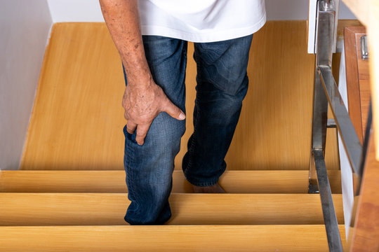 Senior Man Going Up The Stairs At Home And Touching His Knee By The Pain Of Arthritis. Health Care And Medical Concept. World Senior Citizen Day.