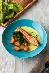 Top view of a grilled salmon steak with baked baby potatoes, spinach and coconut milk gravy served on a wooden table
