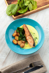 Top view of a grilled salmon steak with baked baby potatoes, spinach and coconut milk gravy served on a wooden table