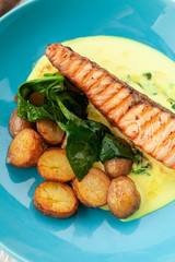 Close up of a grilled salmon steak with baked baby potatoes, spinach and coconut milk gravy served on a bright plate