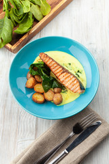 Top view of a grilled salmon steak with baked baby potatoes, spinach and coconut milk gravy served on a wooden table