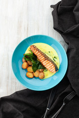 Top view of a grilled salmon steak with baked baby potatoes, spinach and coconut milk gravy served on a wooden table
