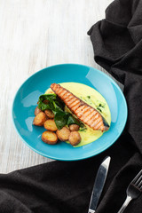 Top view of a grilled salmon steak with baked baby potatoes, spinach and coconut milk gravy served on a wooden table
