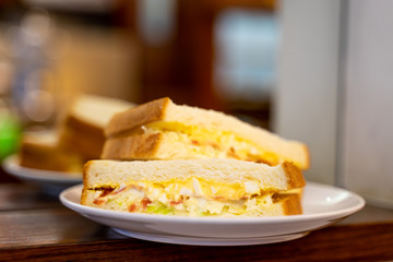 Closed up of morning sandwiches with egg, ham and vegetable on white dish in coffee shop