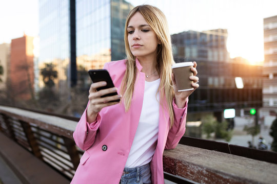 Young businesswoman using smartphone and holding coffee to go