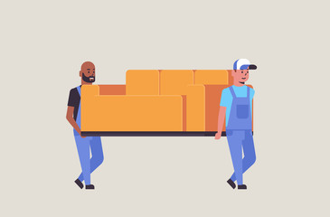 two mix race couriers in uniform moving couch express delivery service concept professional furniture movers holding new sofa flat full length horizontal