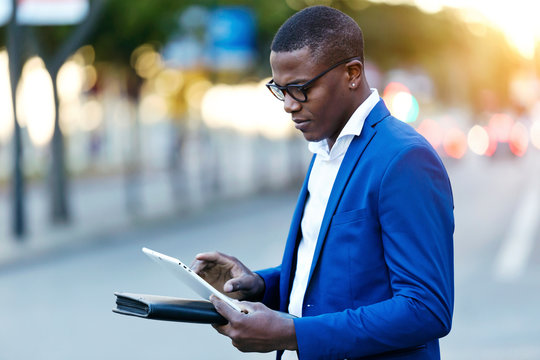 Young businessman wearing blue suit jacket and using his digital tablet at a street