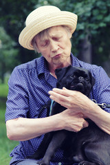 Portrait of elderly woman holds a small dog in her arms and talks to dog. The dog is showing emotions. The breed of dog is a pug.