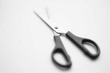 Open scissors with a black handle lie on a white surface
