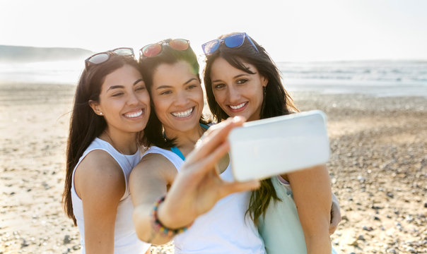 Portrait of happy female friends taking a selfie on the beach