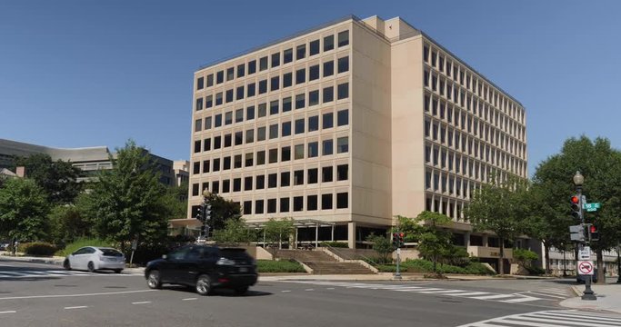 A daytime exterior establishing shot of a typical Washington, D.C. office building as traffic passes by.  	