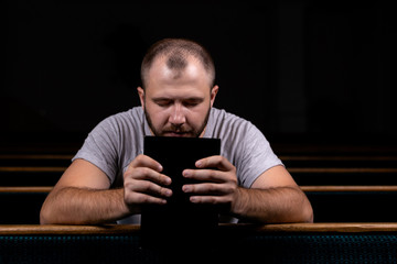 A young guy sits on a church bench, reads the bible and prays. The concept of religion, prayer,...