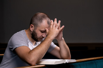 A young guy sits on a church bench, reads the bible and prays. The concept of religion, prayer,...
