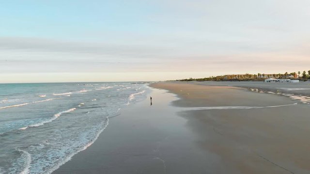 aerial view of a sunrise on the beach of rota, cadiz, you can see 3 people sitting on the sand and another person walking, in the fodo you see houses and trees. The sun is at the bottom,man fishing
