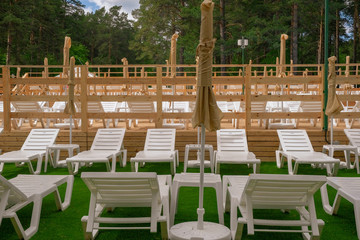 white plastic sun loungers for relaxing and sunbathing in the fresh air by the pool, an umbrella for sun protection, on wooden floors