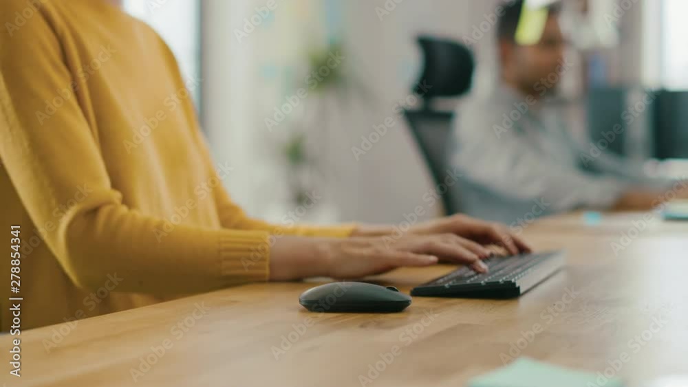 Poster anonymous young woman sitting at her desk using laptop computer. focus on hands typing on keyboard. 
