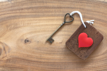 House key in heart shape with home keyring on old wood background decorated with mini heart