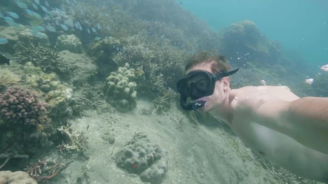 Man is snorkeling in ocean among coral reefs shooting himself on action camera.