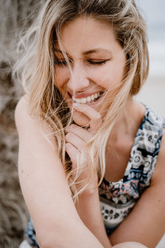 Pretty blonde woman in top biting forefinger and smiling with closed eyes on nature background