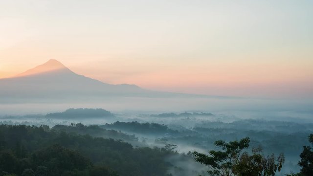 Sun ricing over Mount Merapi, overlooking the Buddhist temple Borobudur, lost in the early morning swirling mist.