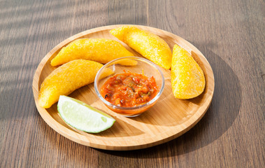 Colombian empanada with spicy sauce on wooden background