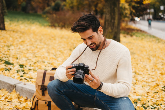 Side view of handsome young photographer in autumn park and watching pictures on camera
