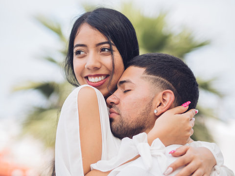 Young handsome man with closed eyes embracing attractive smiling woman
