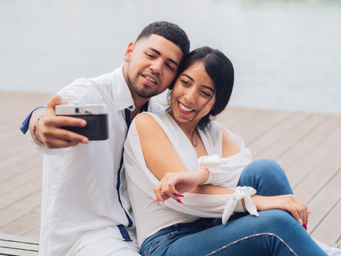Young couple sitting and having fun taking a selfie picture on wooden bench on sandy seaside and kissing