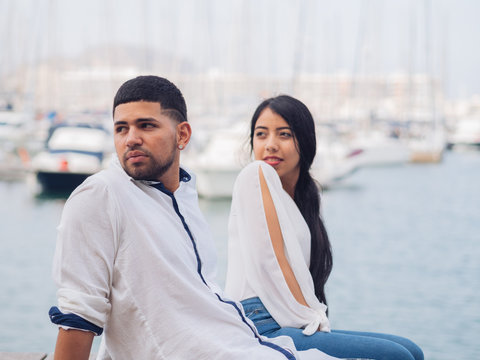 Young handsome man and woman sitting on wooden surface looking away