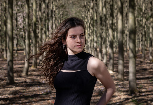 Beautiful young female standing in beautiful wood forest full of tall trees on the background and looking away