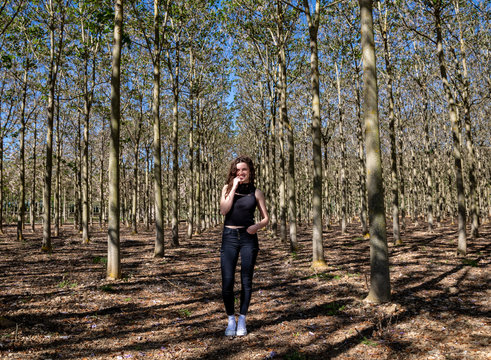 Beautiful young female standing in beautiful wood forest full of tall trees on the background and looking away