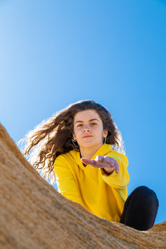 From below brunette woman in yellow sweatshirt giving hand in sandstone rocks on blue sky background